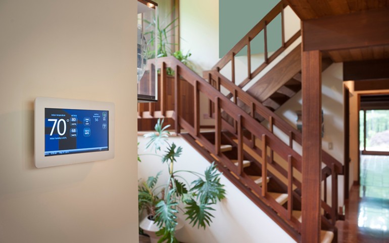 Smart thermostat on a wall next to stairs.